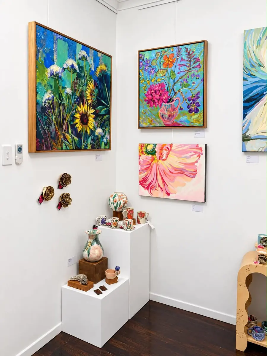 Sunflower and floral paintings above a small display of ceramics