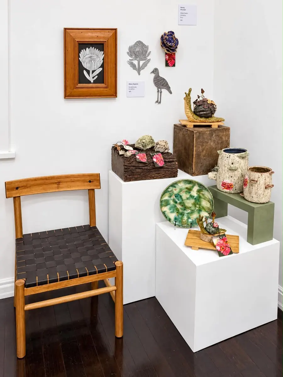 A small framed work, ceramics and a timber chair beside a plinth