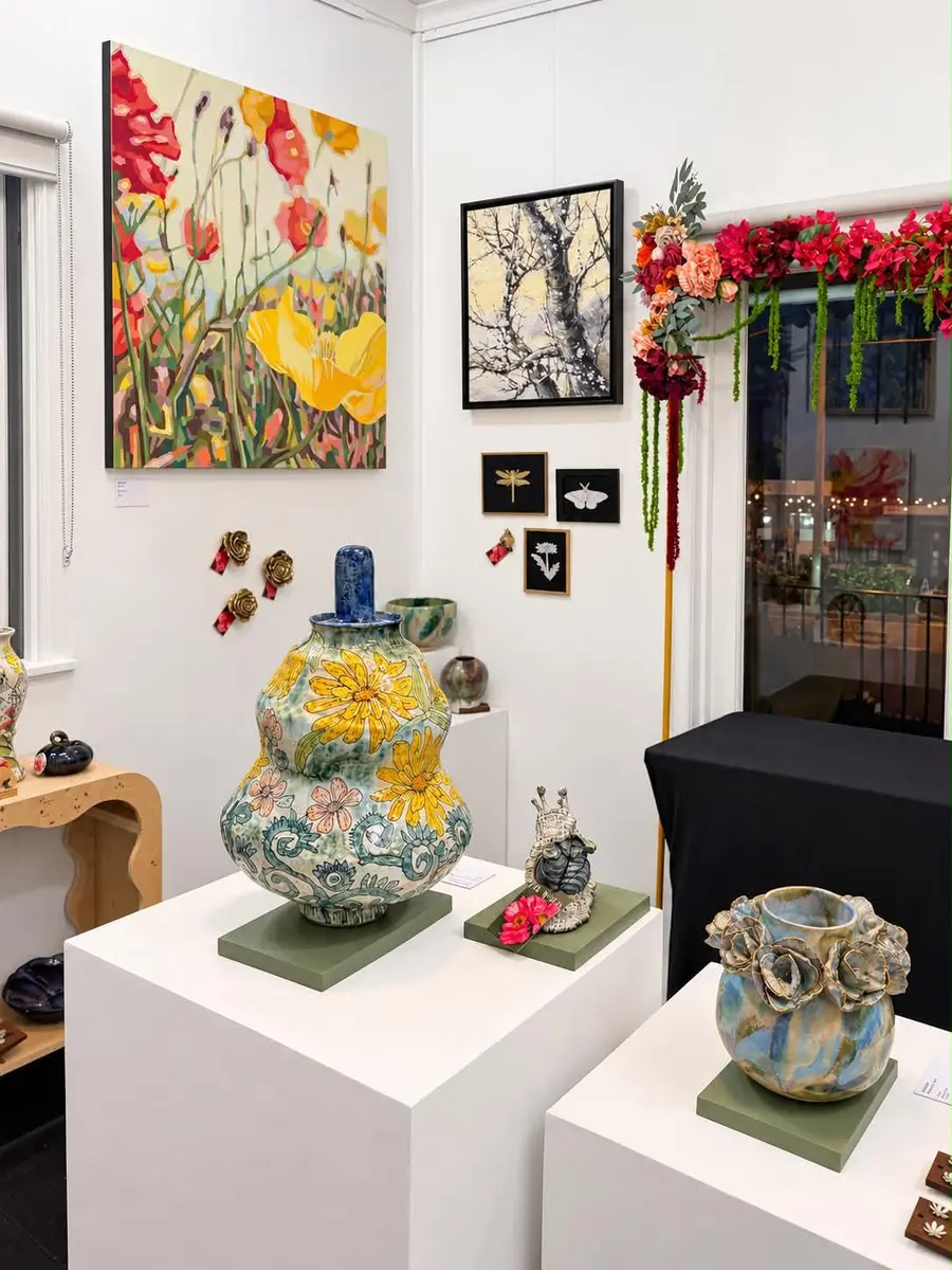 A decorated vase on a plinth below floral paintings