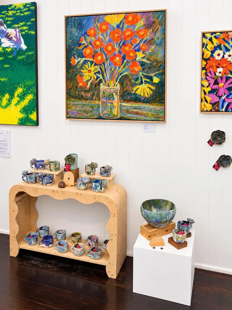 An orange flower painting above a console of cups and bowls